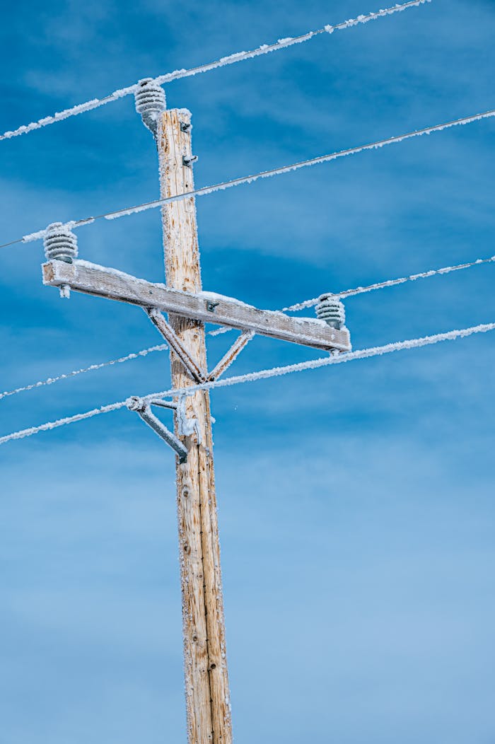 our-story Wooden electric pole with snow-covered power lines against a blue sky.